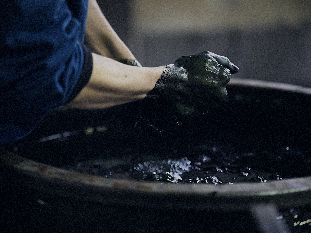 Indigo-stained hands wringing cloth over the dye vat