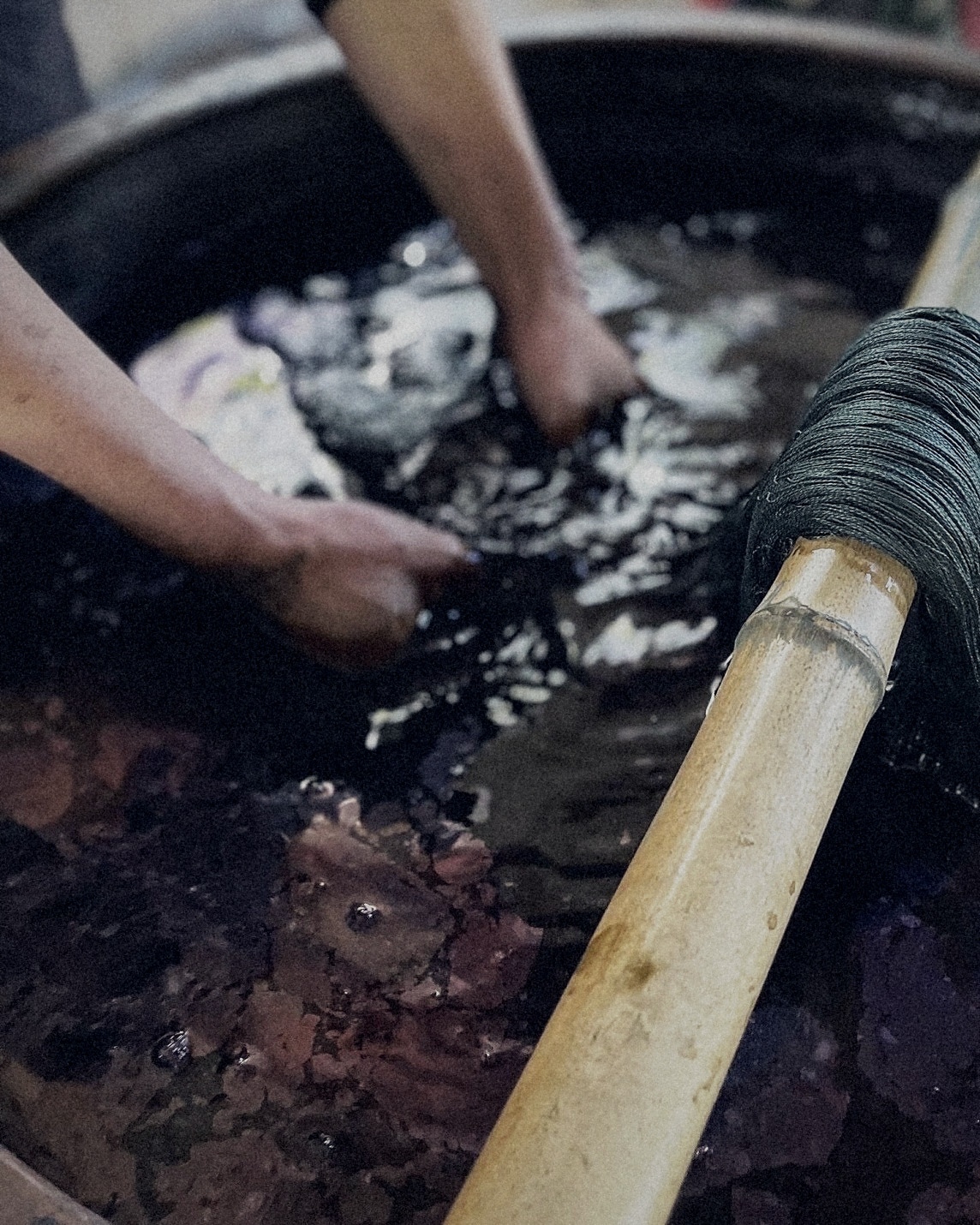 Hands working dyed thread in a natural indigo vat