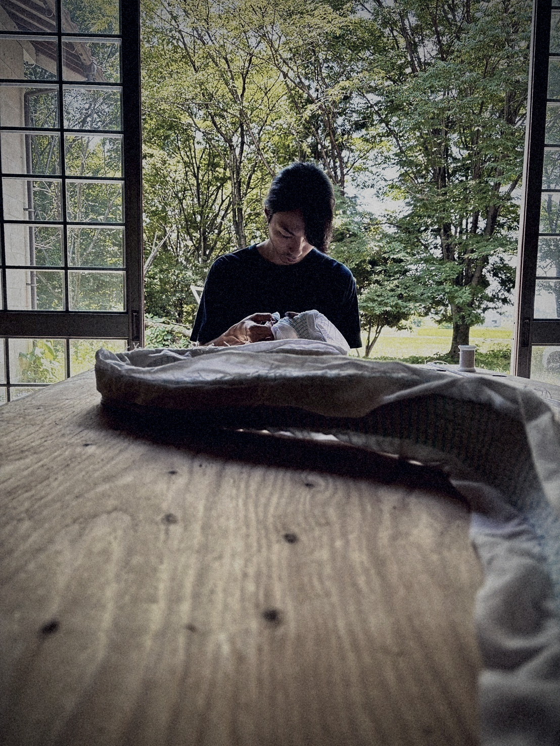 Artisan stitching cloth beside open shoji doors, rice fields beyond